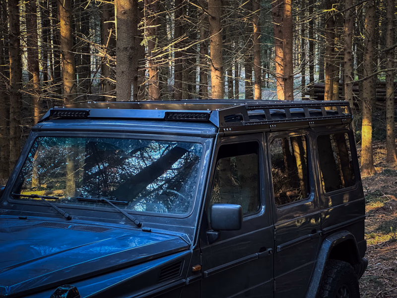 Dark G-Class with Walger Works roof rack, 3/4 view in forest